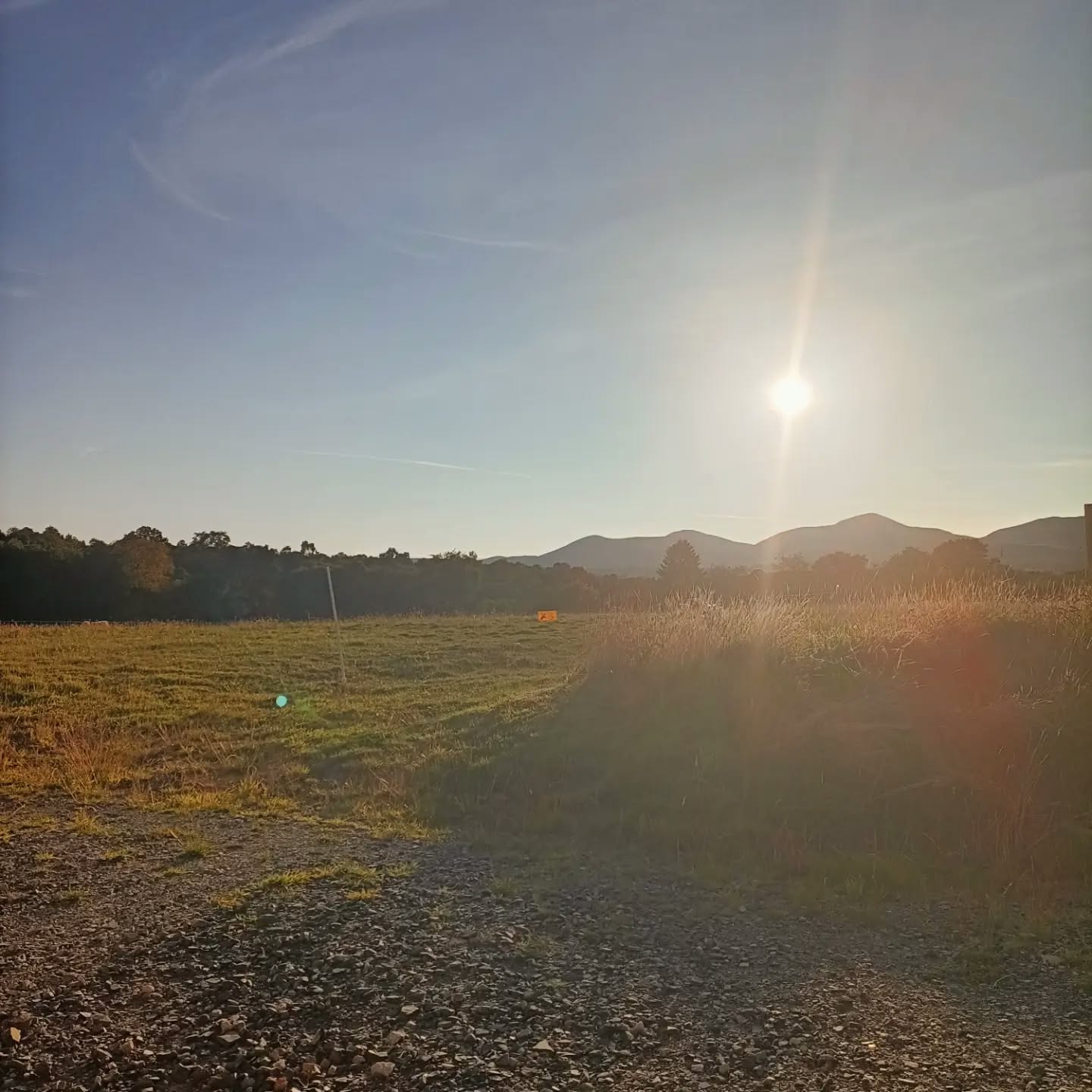 Un champ fauché et des herbes hautes au soleil bas, des collines à l’horizon